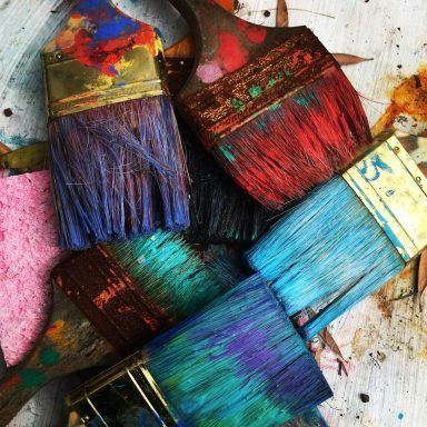 Bunte Pinsel Bunte Pinsel mit verschiedenen Farbtönen auf einer rustikalen Unterlage.
